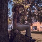 A young woman in a straw hat sits on a tree stump, enjoying a sunny day in Chascomús, Argentina.