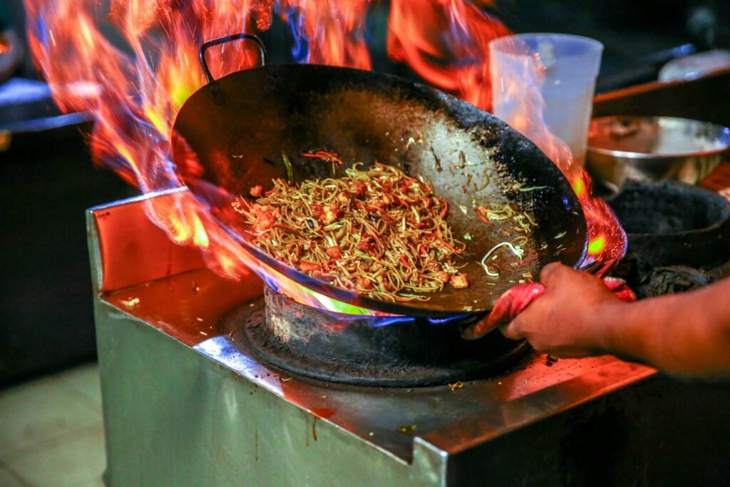 Vibrant close-up of chef cooking noodles in a flaming wok inside a restaurant kitchen.
